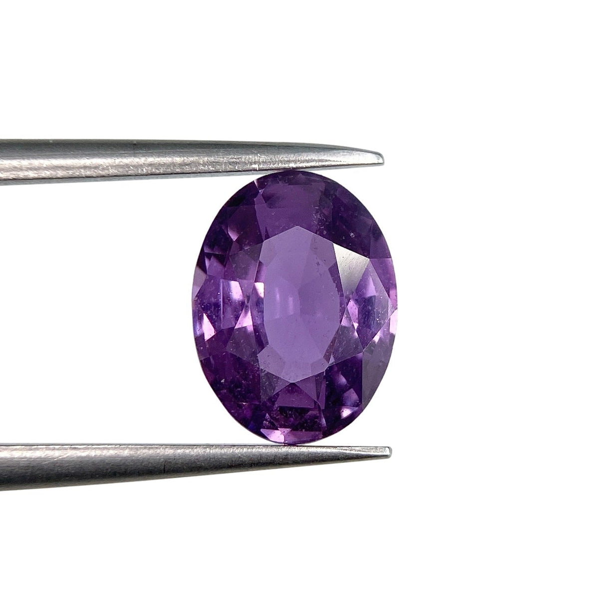 2.02ct oval brilliant cut pinkish-purple sapphire held in metal tweezers against a white background.