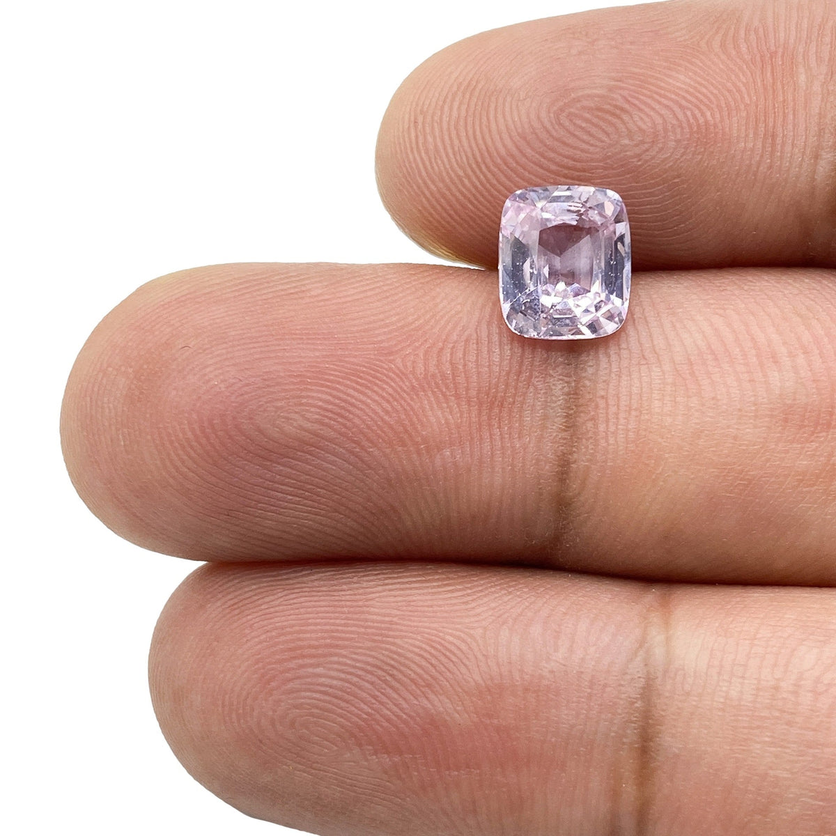 2.04ct brilliant cut cushion-shaped pink sapphire held between fingers, showcasing its light pink color and faceted design.