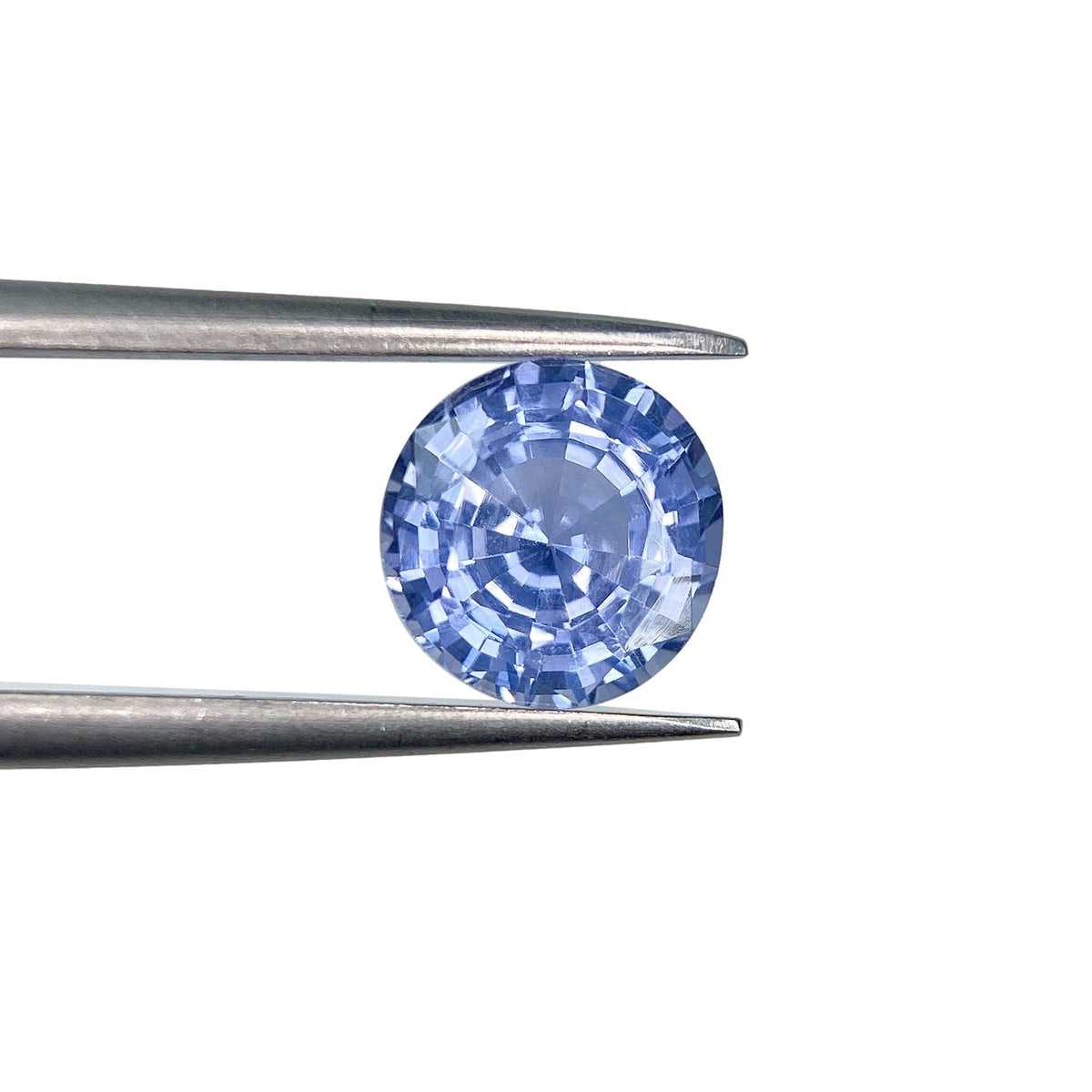 2.05ct round brilliant cut blue sapphire held by metal tweezers against a white background.