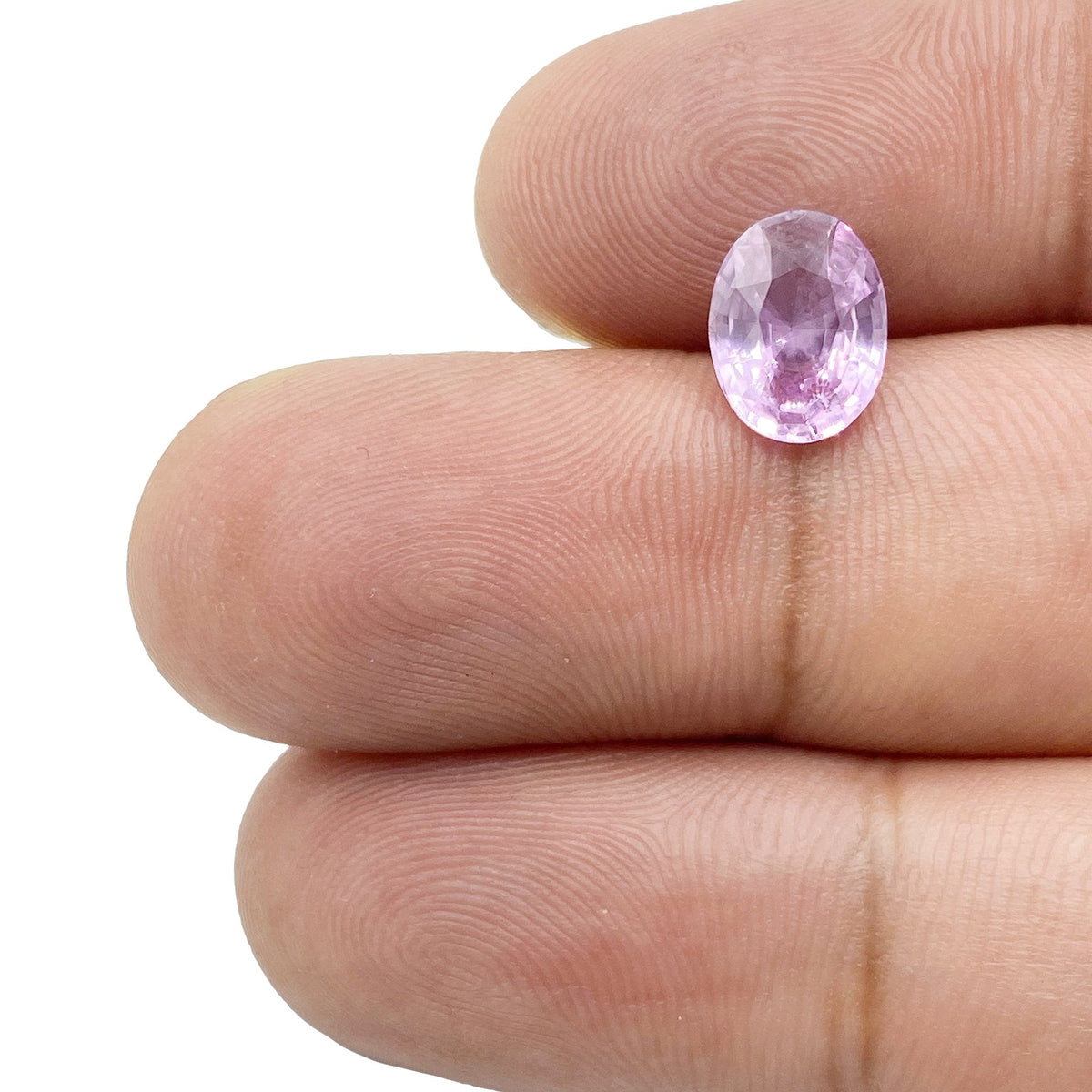 2.06ct oval brilliant cut pink sapphire gemstone held between fingers, showcasing its faceted clarity and light pink hue.