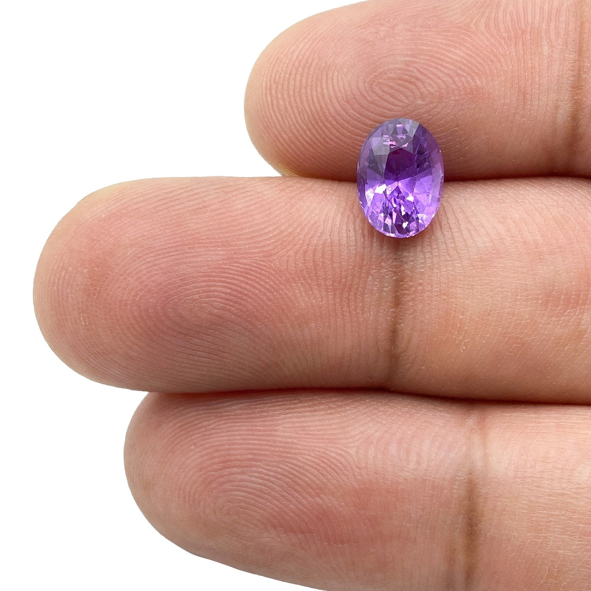 2.07ct brilliant cut oval violet sapphire gemstone held between fingers, showcasing vibrant purple facets.