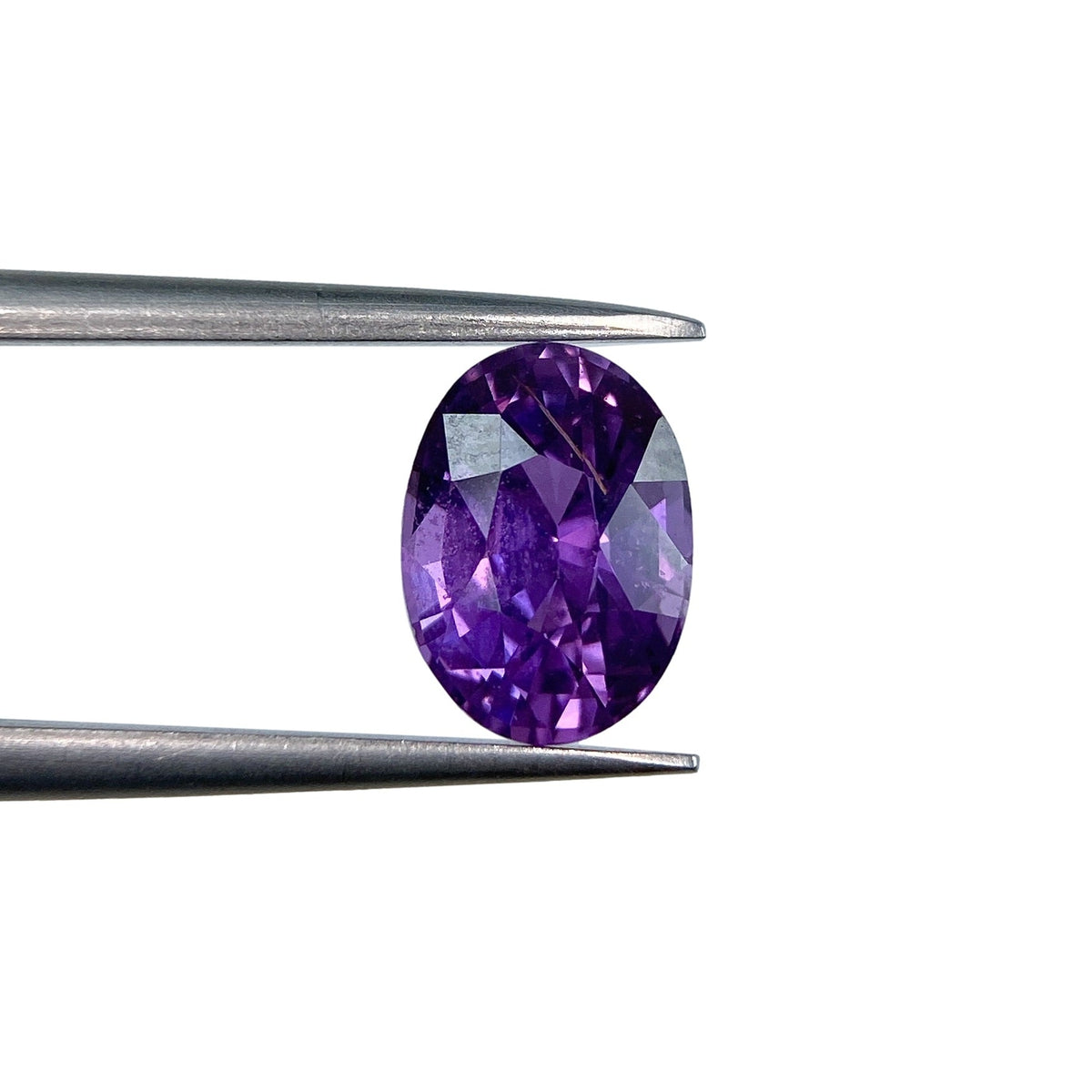 2.07ct brilliant cut oval violet sapphire held in metal tweezers against a white background.