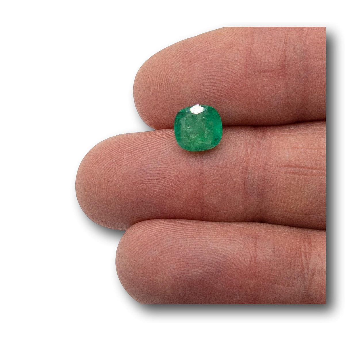 2.08ct cushion-cut Muzo emerald with a brilliant facet pattern held between fingers.