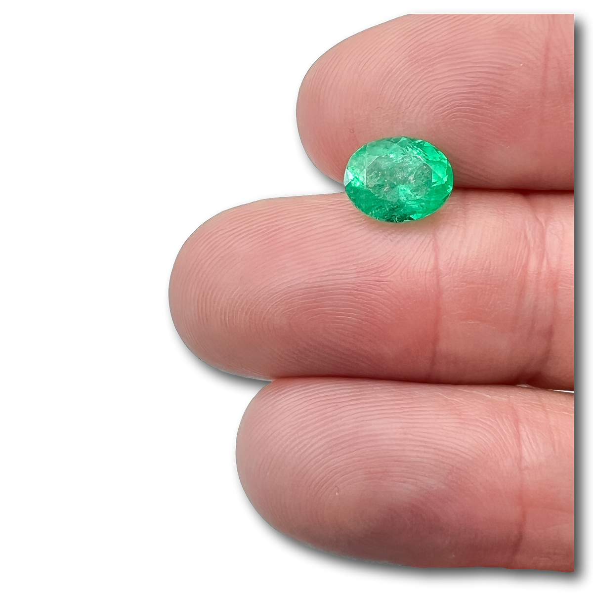 2.20ct oval brilliant cut Muzo emerald held between fingers, showcasing vibrant green color and faceted gemstone texture.