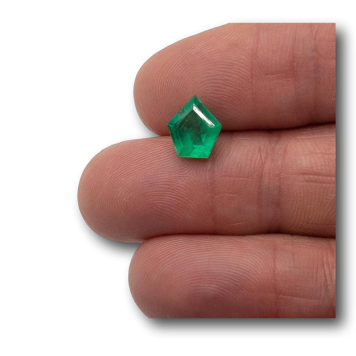 2.21ct Muzo emerald with a step-cut shield shape held between two fingers.