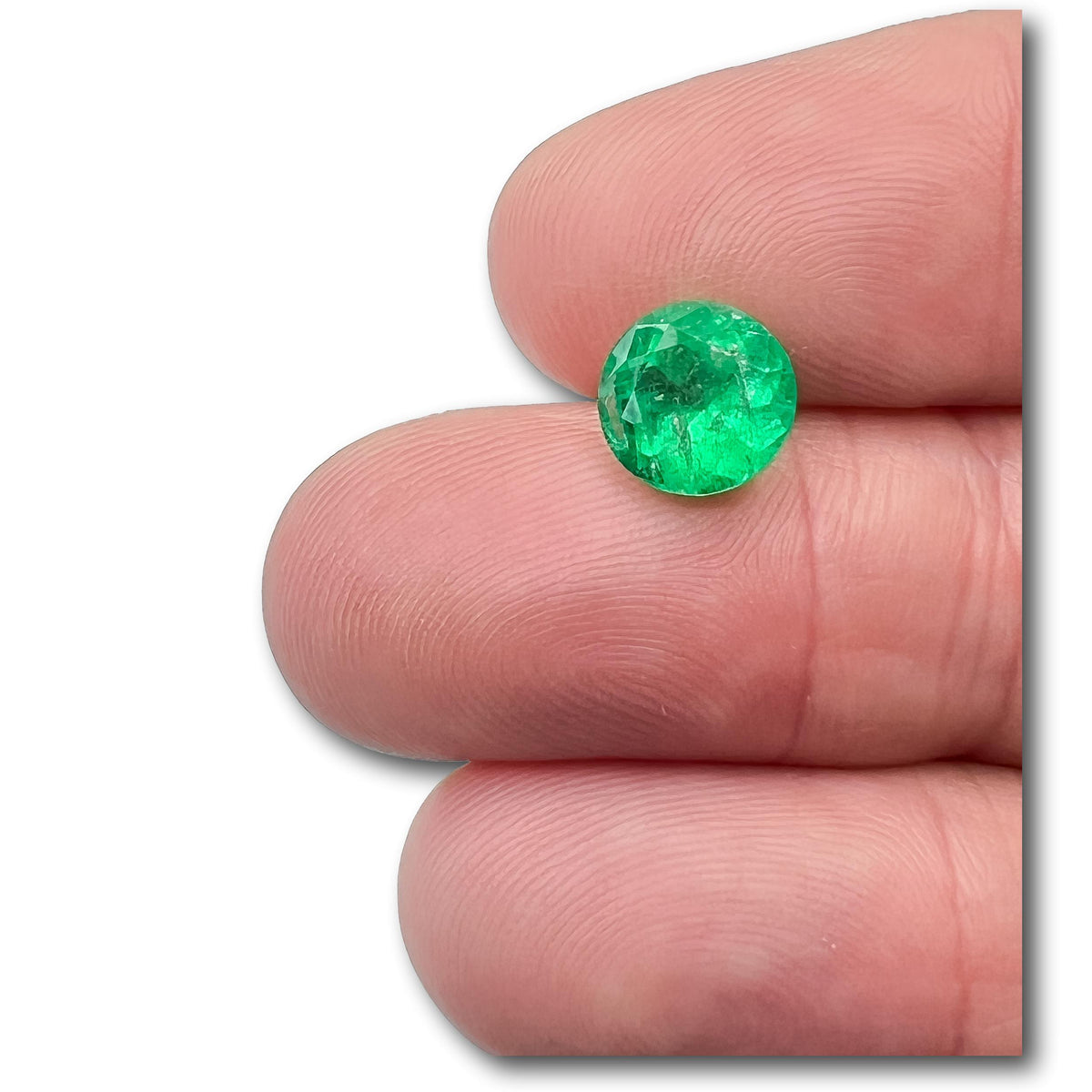 2.24ct round brilliant cut Muzo emerald with vibrant green color held between fingers.