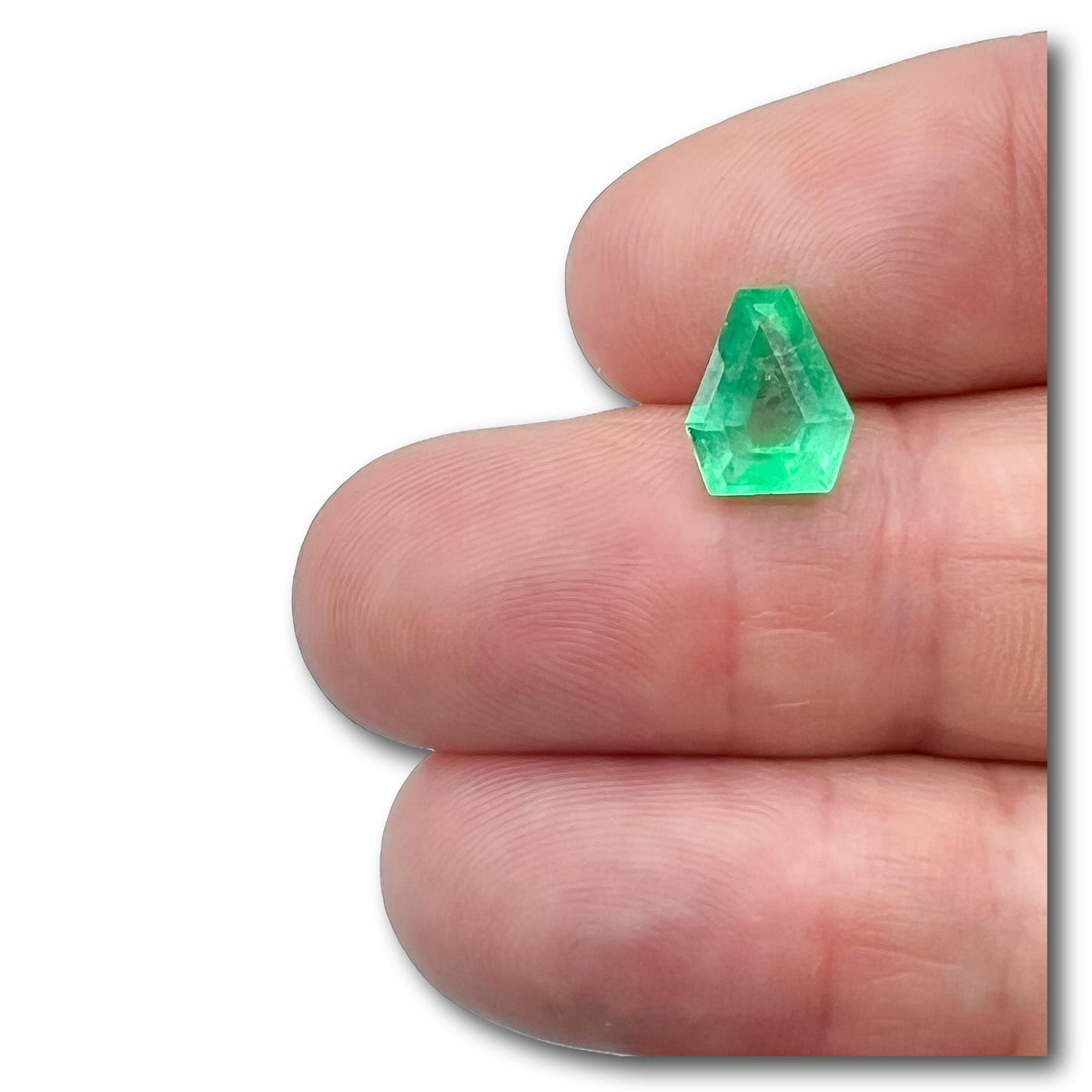 2.28ct Muzo Colombian emerald with a step-cut shield shape held between fingers.