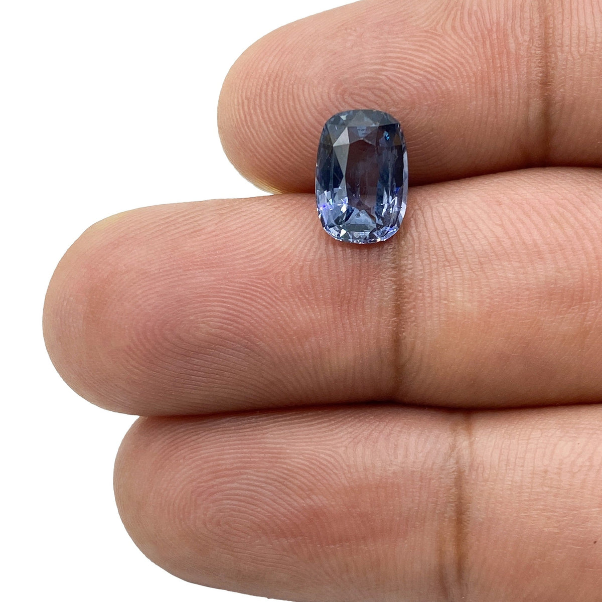 2.39ct brilliant cut cushion-shaped blue spinel gemstone held between fingers.