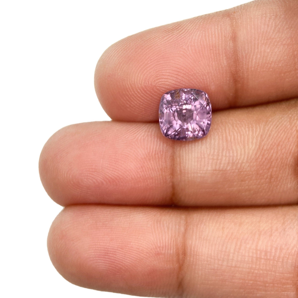 2.57ct brilliant cut cushion-shaped violet spinel gemstone held between fingers.