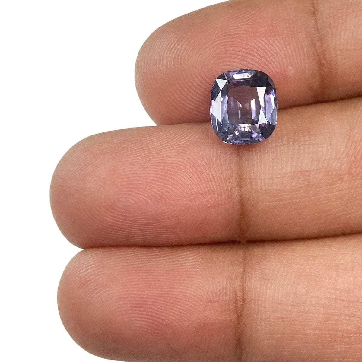 2.58ct cushion-cut purple spinel gemstone with brilliant facets held between fingers.