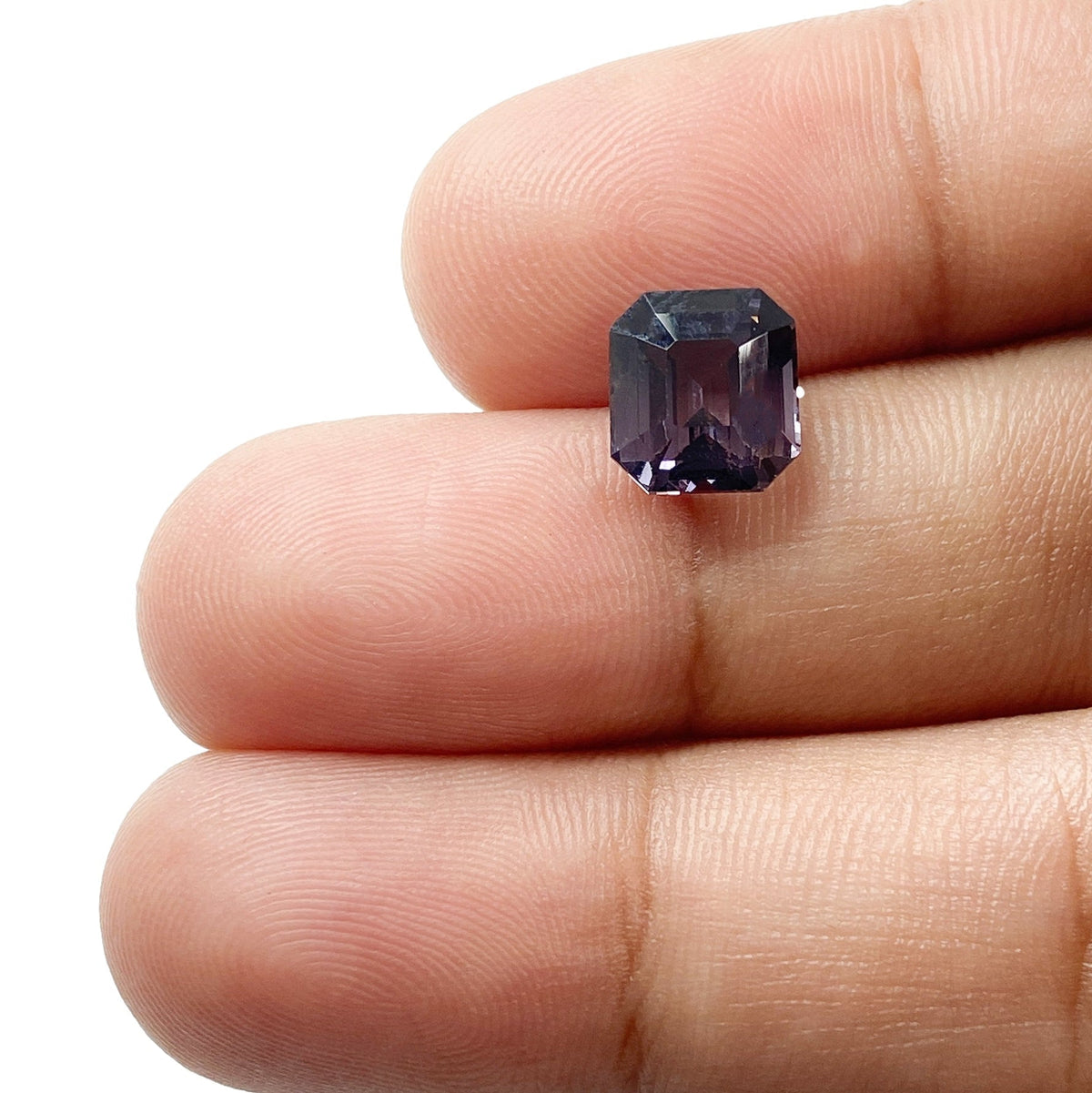 2.63ct emerald-cut pinkish-purple spinel gemstone held between fingers, showcasing its step-cut facets and deep color.