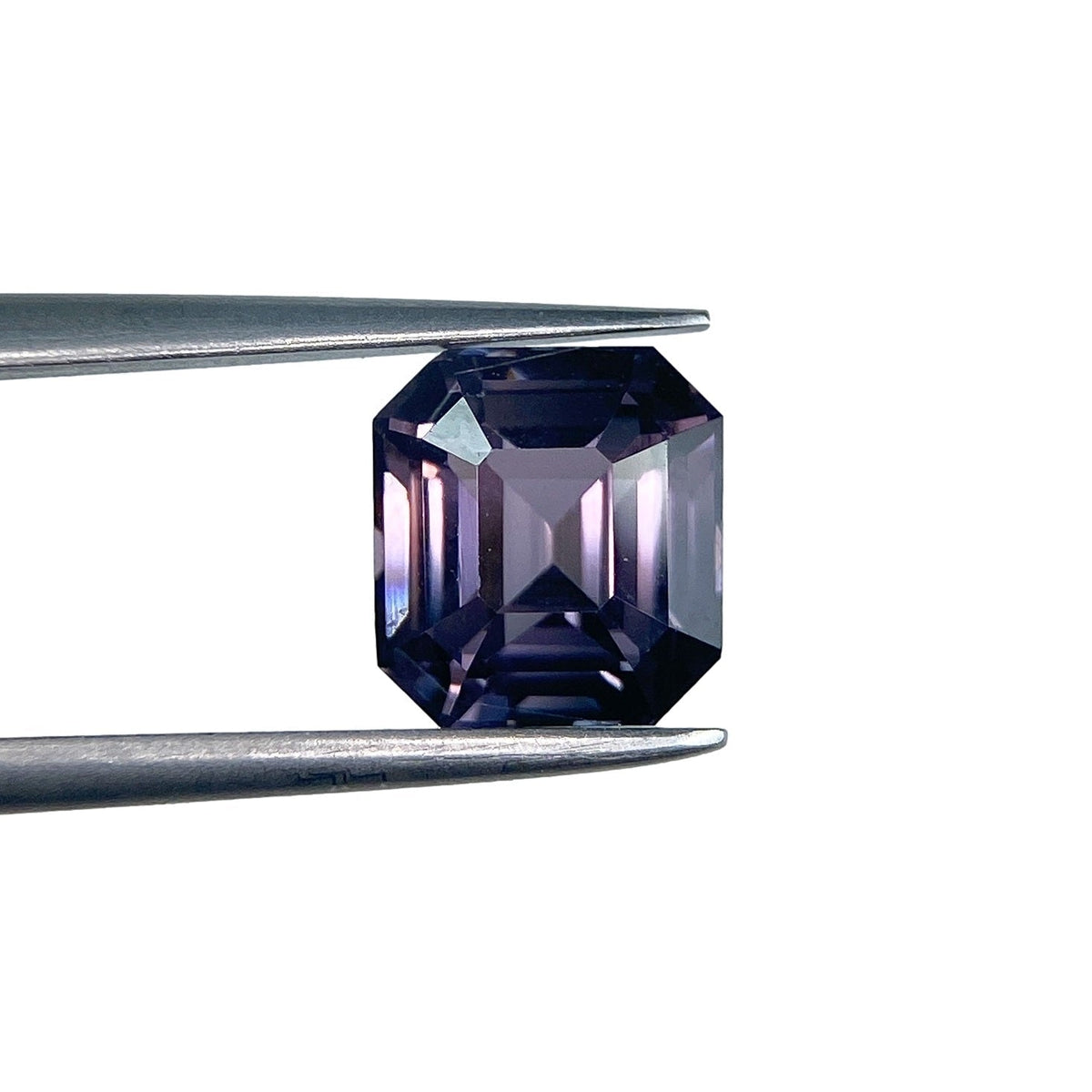 2.63ct emerald-cut purple spinel gemstone held in metal tweezers against a white background.