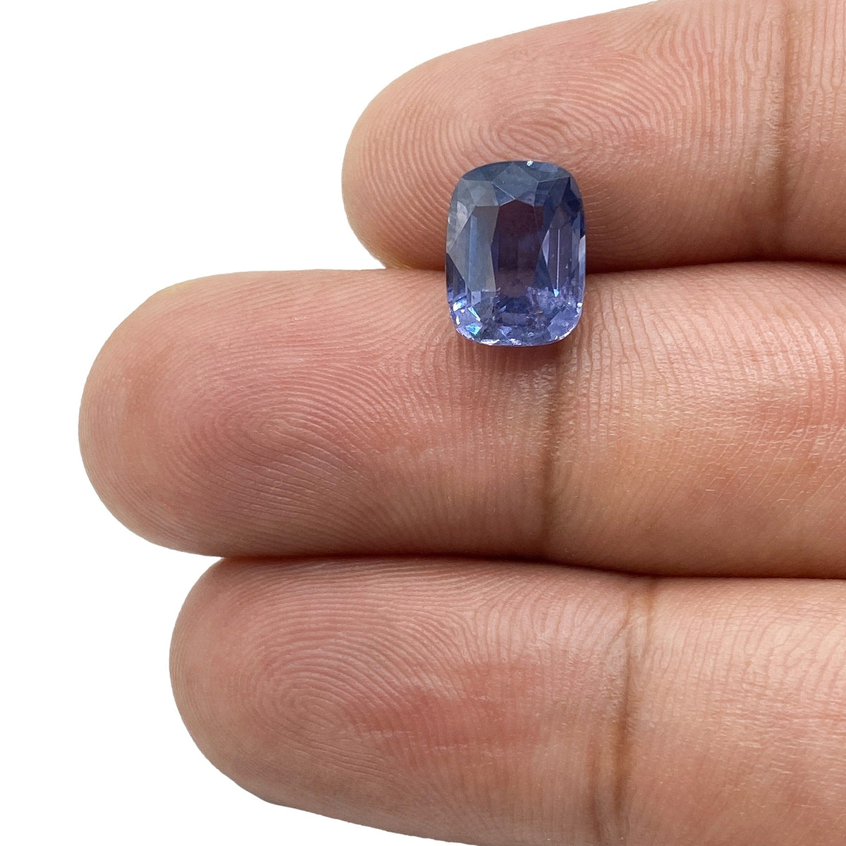 3.07ct brilliant cut cushion blue spinel gemstone held between fingers, showcasing its vibrant color and faceted design.