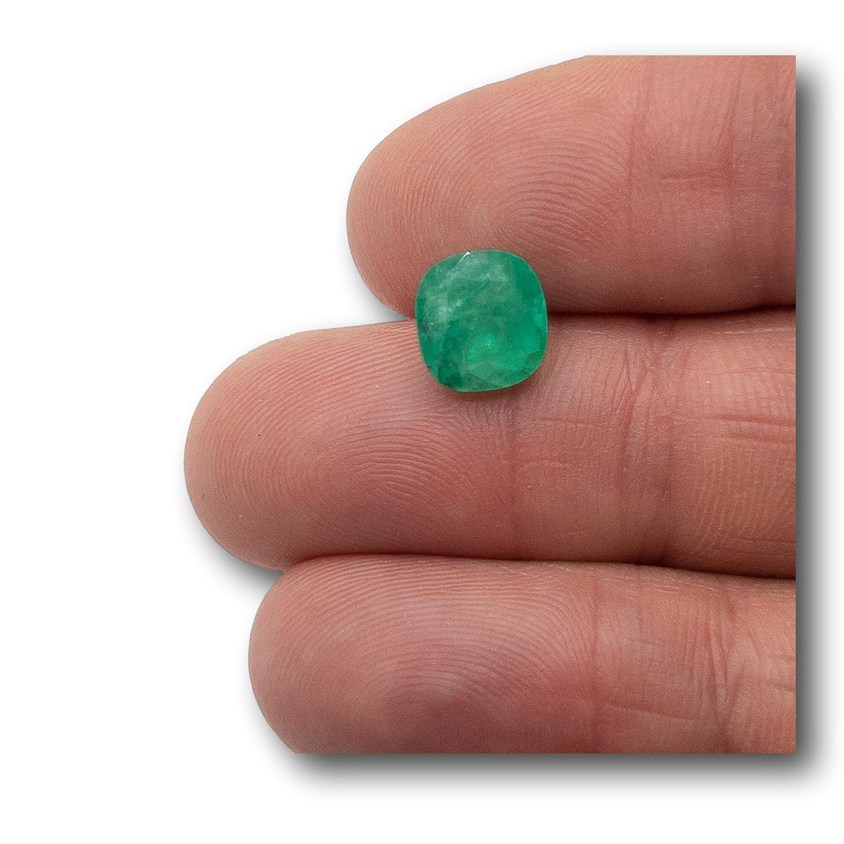 3.10ct cushion-cut Muzo emerald with a vibrant green hue held between fingers.