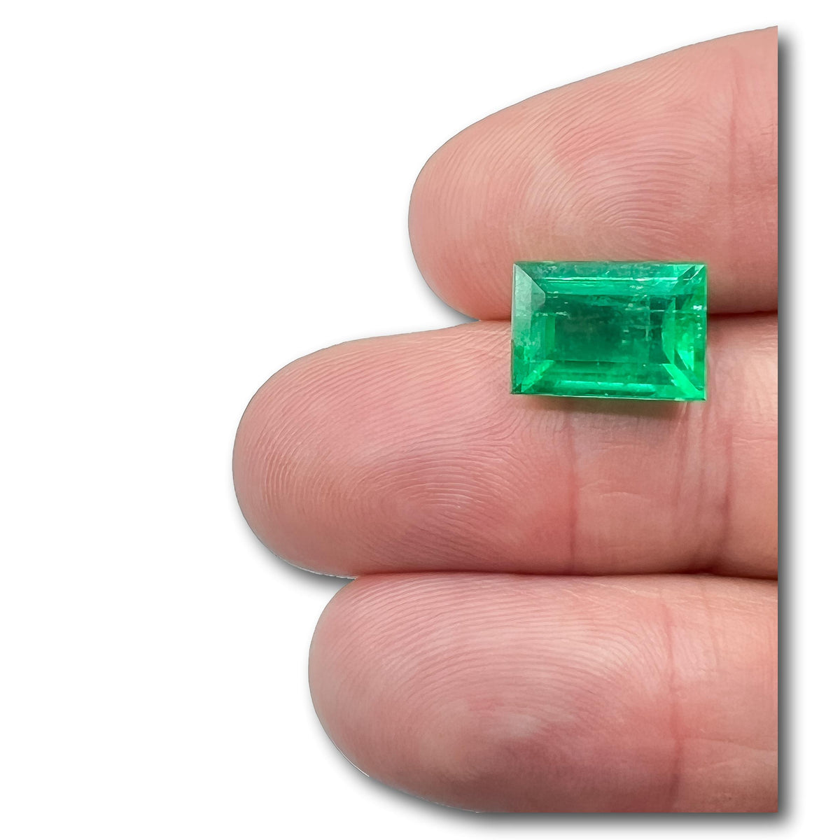 6.20ct Muzo emerald with a step-cut baguette shape held between fingers, showcasing a vibrant green gemstone.
