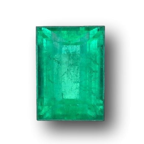 6.20ct Muzo emerald with a step-cut baguette shape and vibrant green color against a white background.