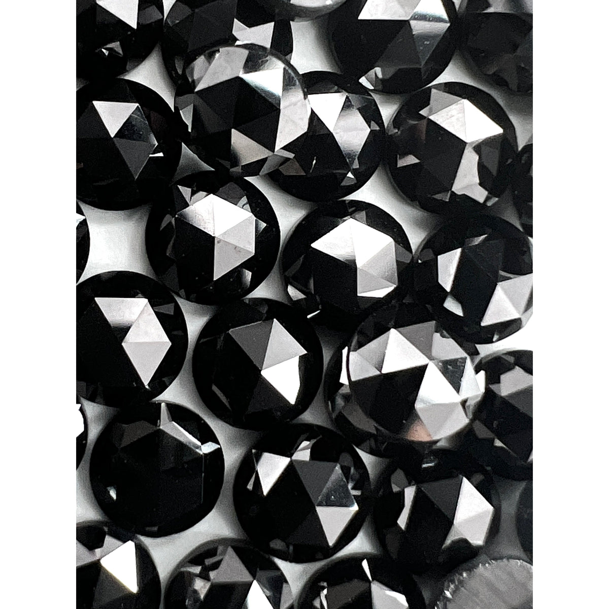 A collection of loose, round black diamond melee stones featuring a faceted rose-cut design with high luster.