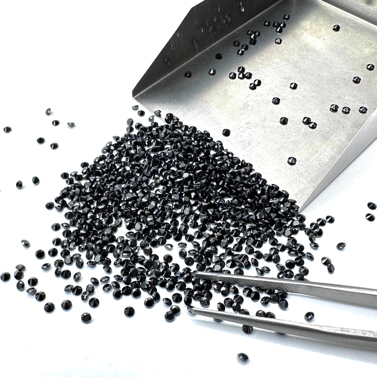 A pile of loose, round brilliant-cut black diamonds being sorted with a metal scoop and professional tweezers.