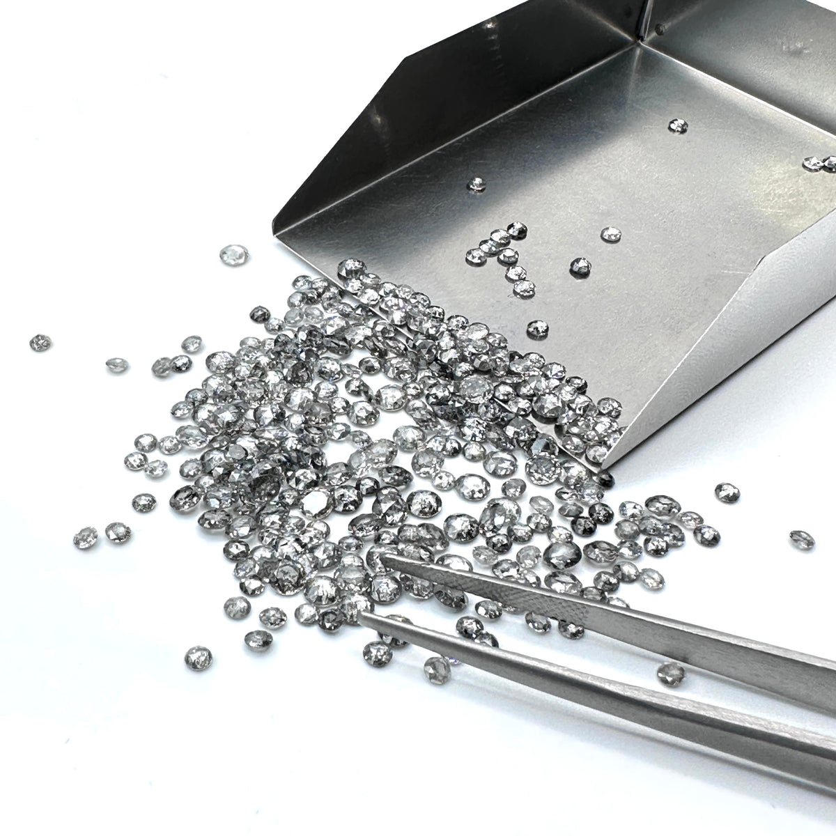 Small rose cut salt and pepper diamond melee stones being sorted with metal tweezers and a diamond scoop.