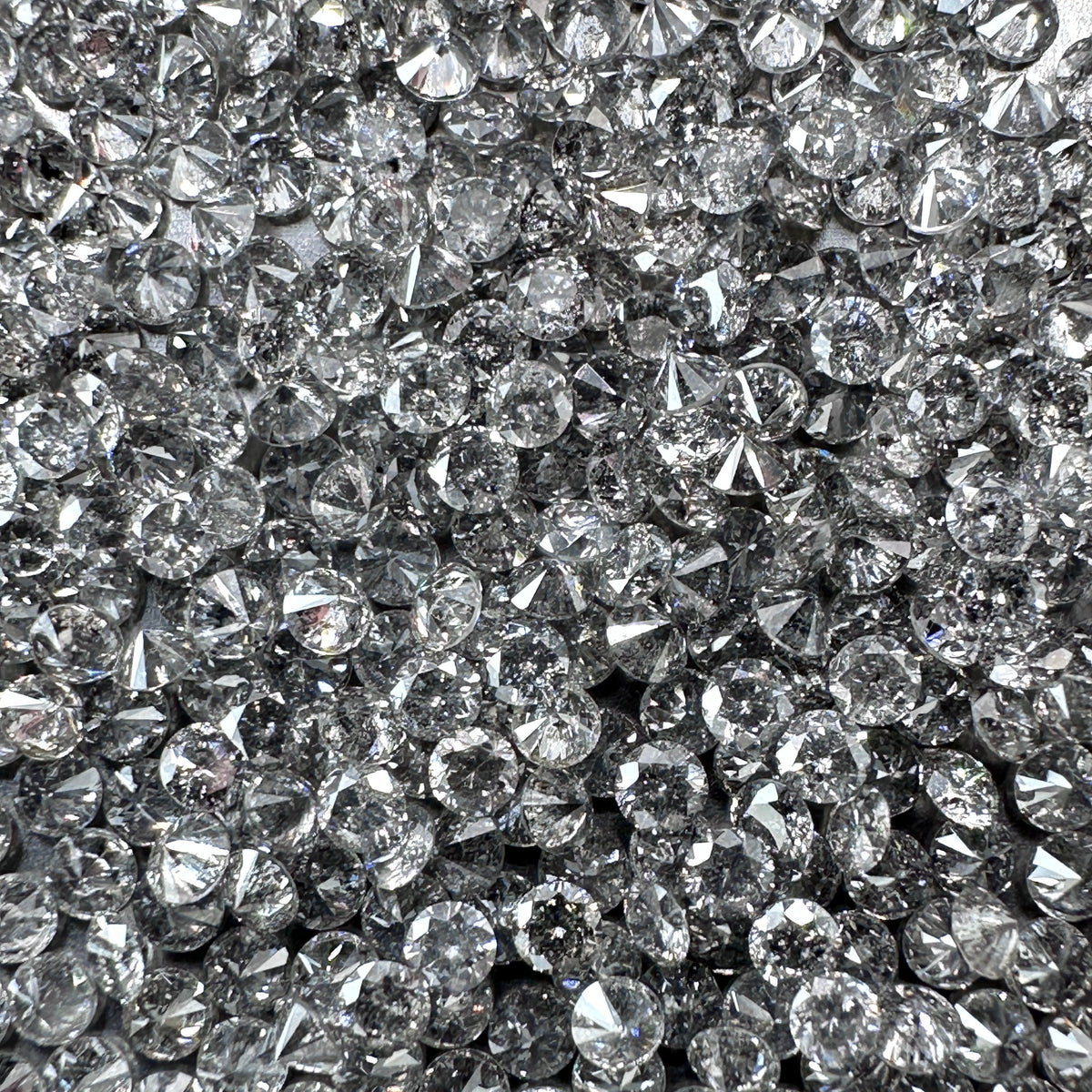 Collection of round brilliant cut salt and pepper diamond melee with natural grey speckled inclusions.